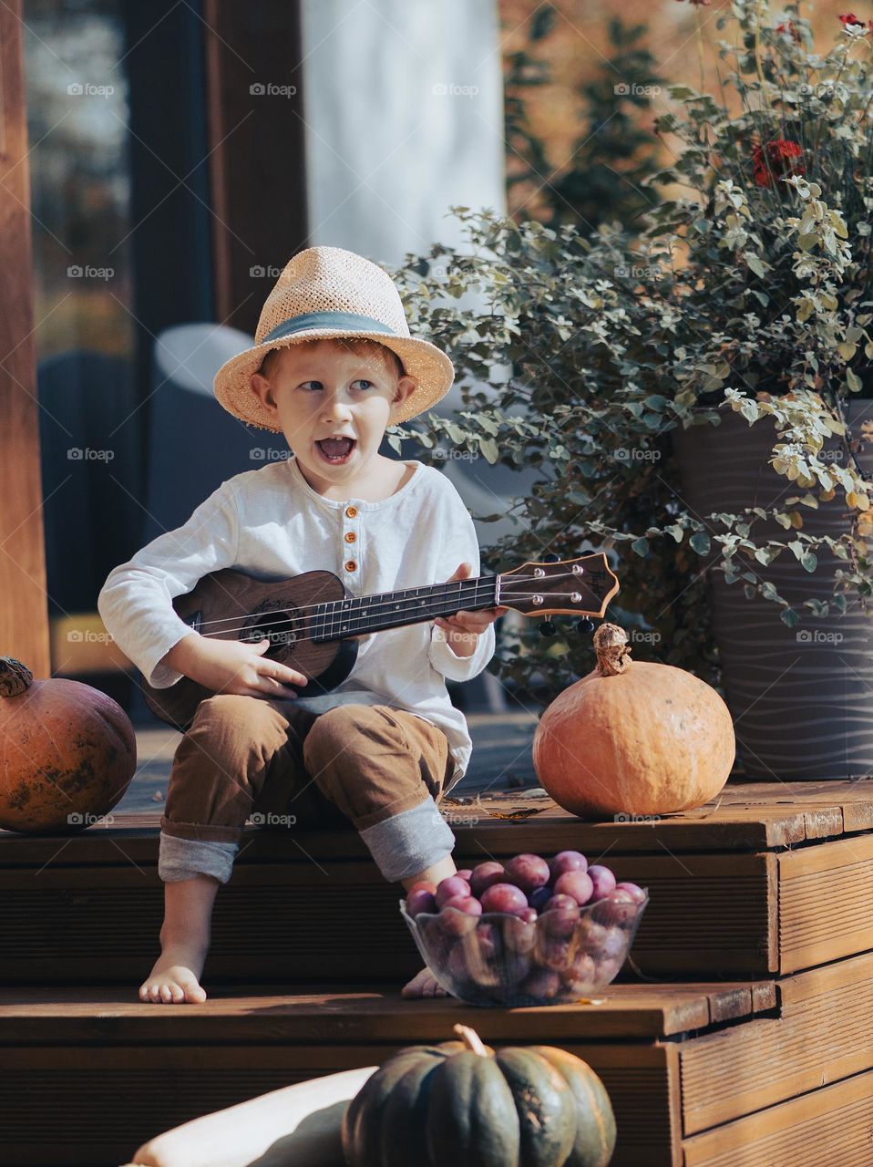 Boy playing guitar while sitting on wooden terrace with pupmkins, autumn vibes