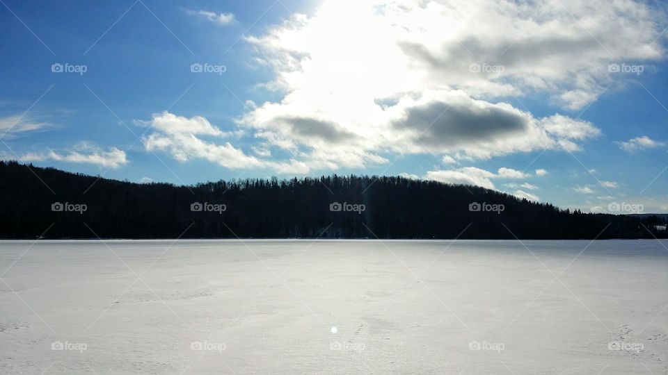 A lake covered with snow during a sunny winter day with mountains and clouds