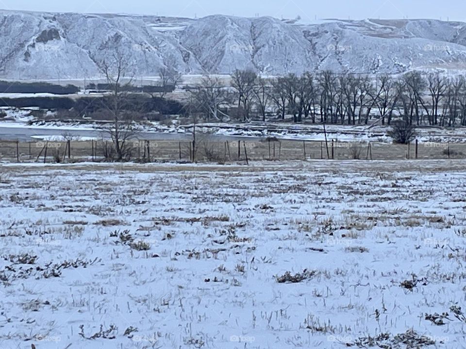 Typical cloudy winter day for Medicine Hat, Alberta, Canada, little snow covering the gold wild grass fields in the foreground, South Saskatchewan river in between, with brown trees and hills of the coulees in the background and a little of the sky
