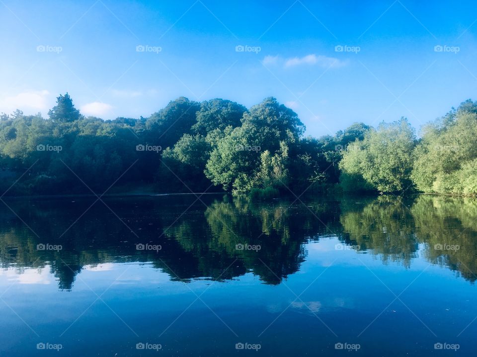 Vale of Health Pond on Hampstead Heath, London. Blue sky and green trees reflected in still water