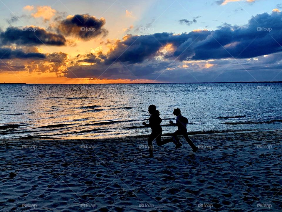 Kids running on the beach as the big orange and crimson ball slowly going down and down and it sets into the horizon making the sky absolutely stunning.