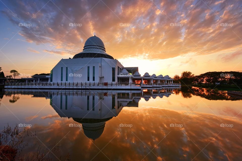Beautiful reflections of the mosque during sunrise with dramatic sky background