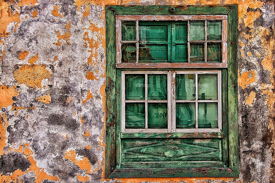 An old weathered green window in a rough broken peeling house wall 