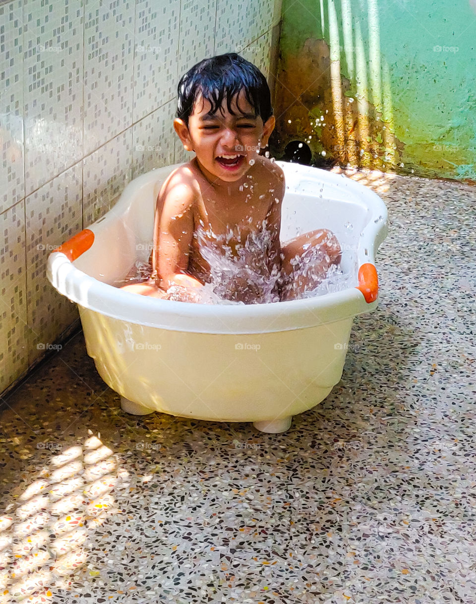 small boy having a splash moment inside his white bathtub in a hot summer day