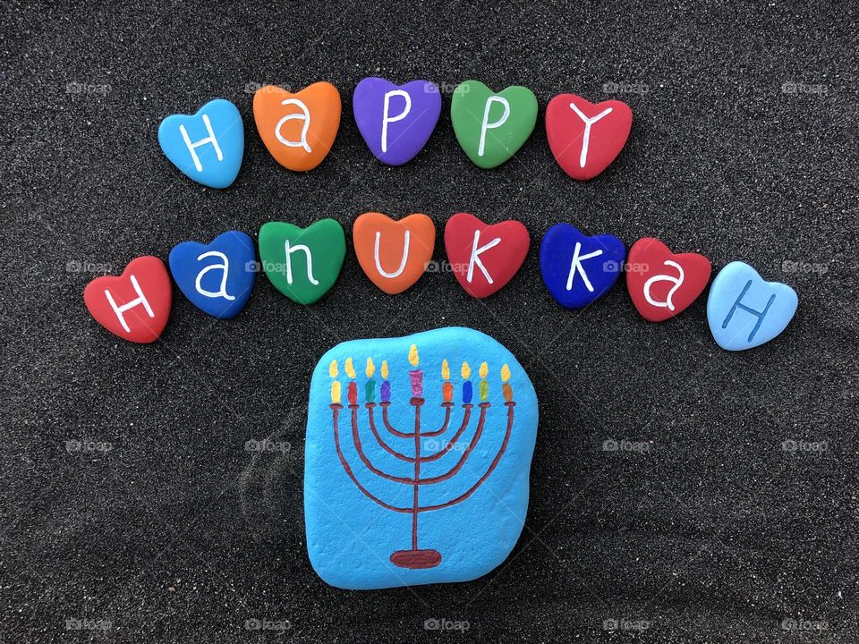 Happy Hanukkah with multicolored heart stones over black volcanic sand
