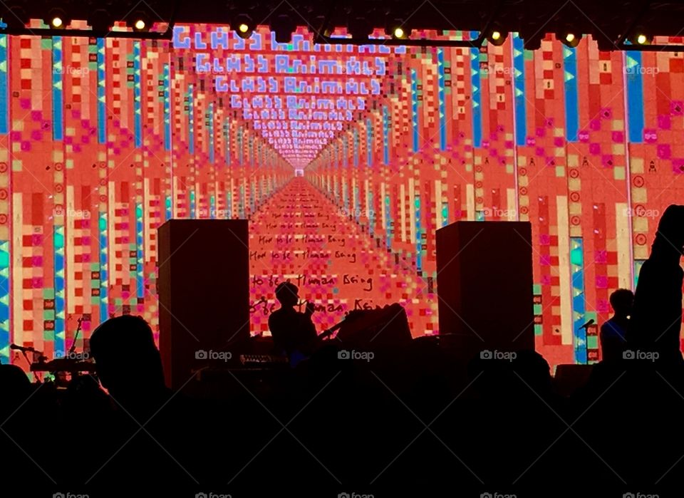Concert stage with lit red screen background and audience silhouette in foreground 