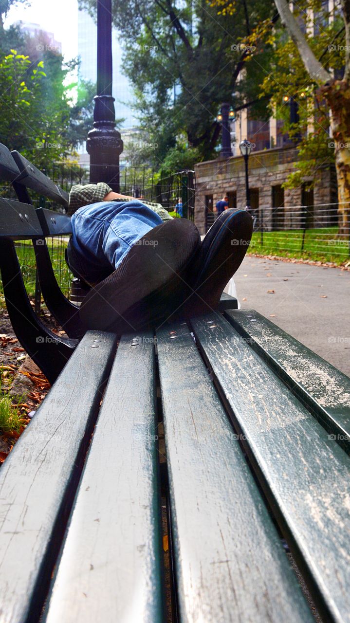 An adult person is seen from low, feet perspective napping on a NYC, Central Park bench