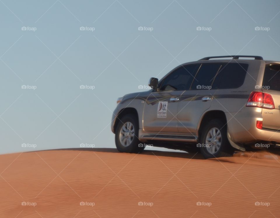 A vehicle gracing the blood orange sands od the desert under a clear sky.