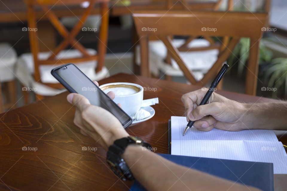 Man’s hands with smartphone and notebook in cafe