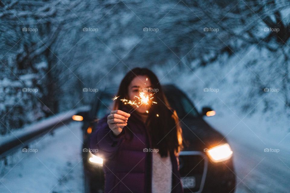 Woman holding sparklers in her hand, while being on a snow covered road.