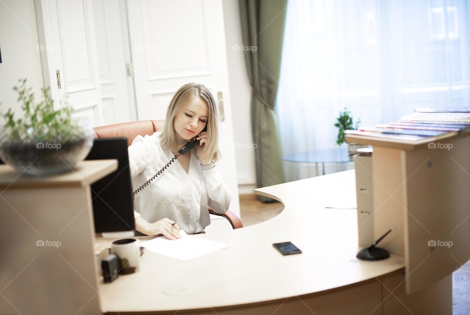 Young female receptionist talking on phone in office