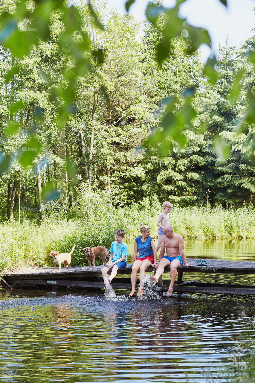 Family spending time together sitting on a bridge over a lake, among the trees, close to nature, during summer vacations. Candid people, real moments, authentic situations