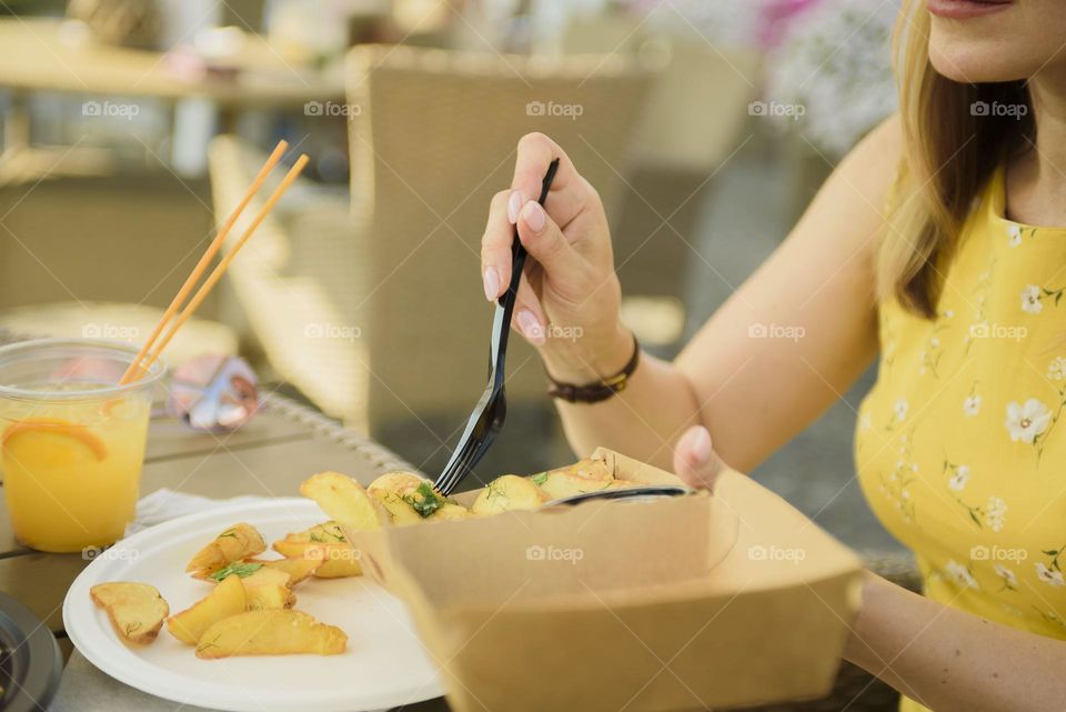 Food using disposable tableware. Black disposable fork with a slice of fried potatoes. Summer street food. Lunch at a summer restaurant in the era of a pandemic.