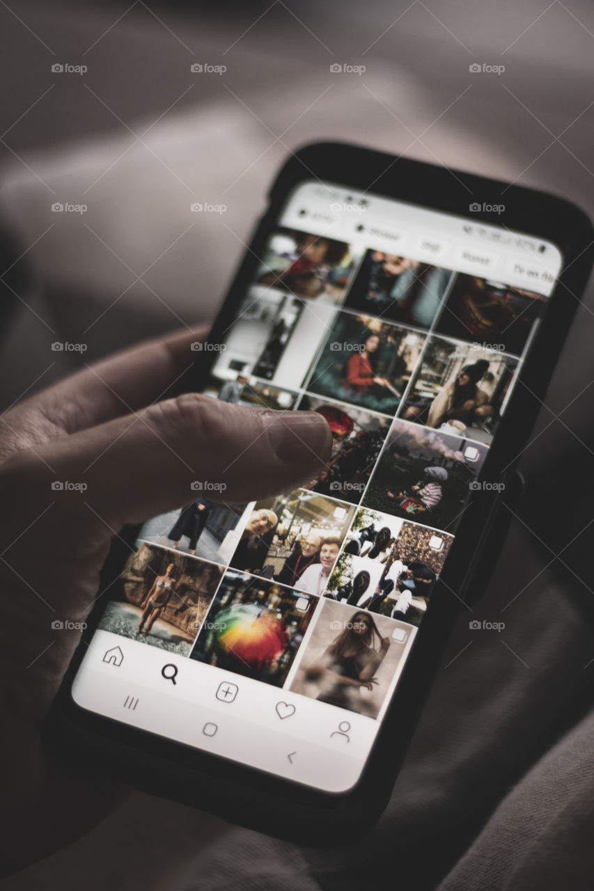 A portrait of someone using a Samsung smartphone and holding in his or her hand, using the Instagram application, browsing through photos.