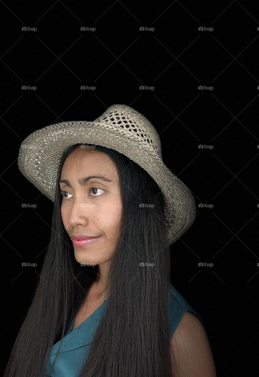 Portrait of young adult woman with long hair wearing a gray hat with black background.