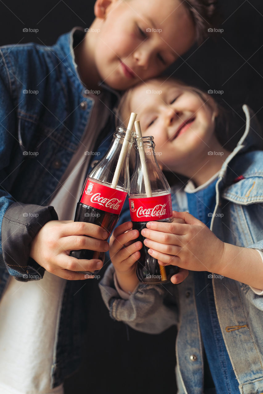 beautiful, stylish, fair-haired children, drinking Coca Cola, eating potatoes, dressed in denim clothes, free photo style.  boy and girl have fun, rejoice, beautiful advertisement for coca cola drink