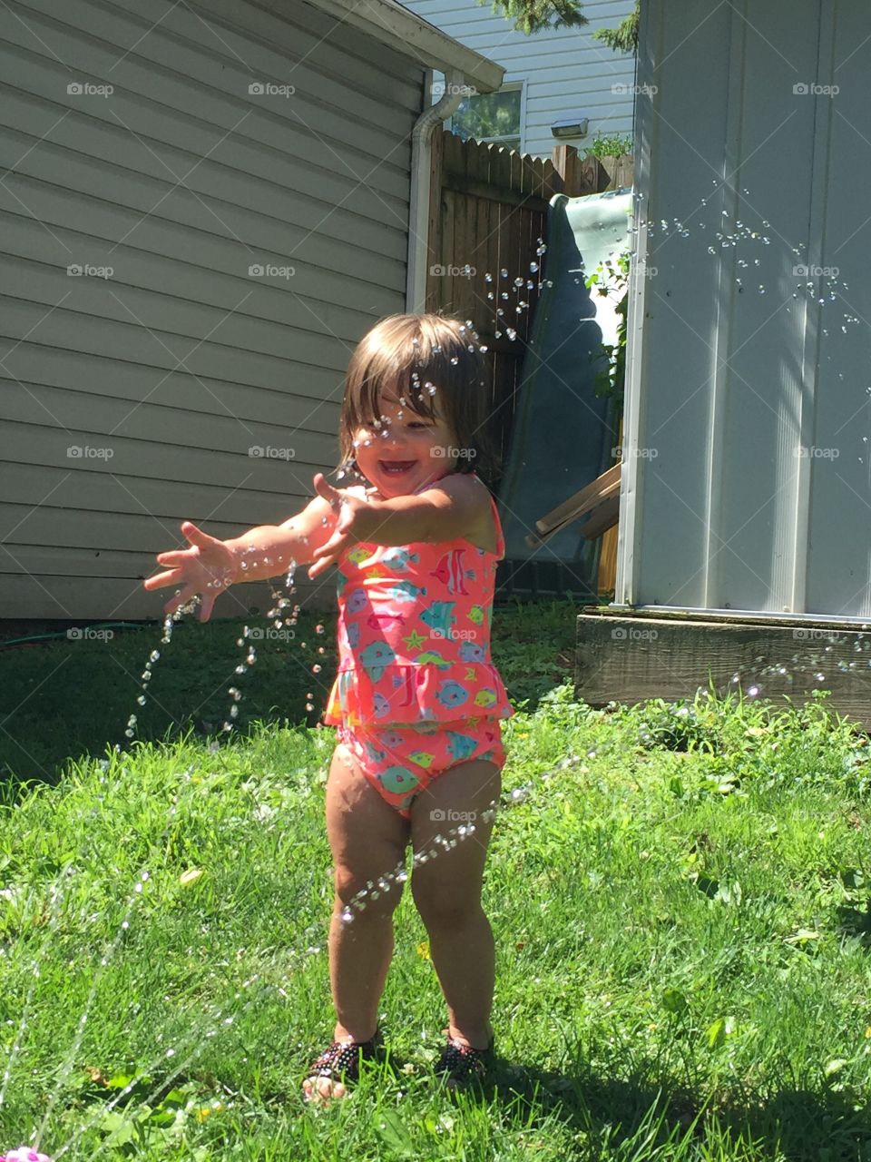 Water splashing on little girl at backyard