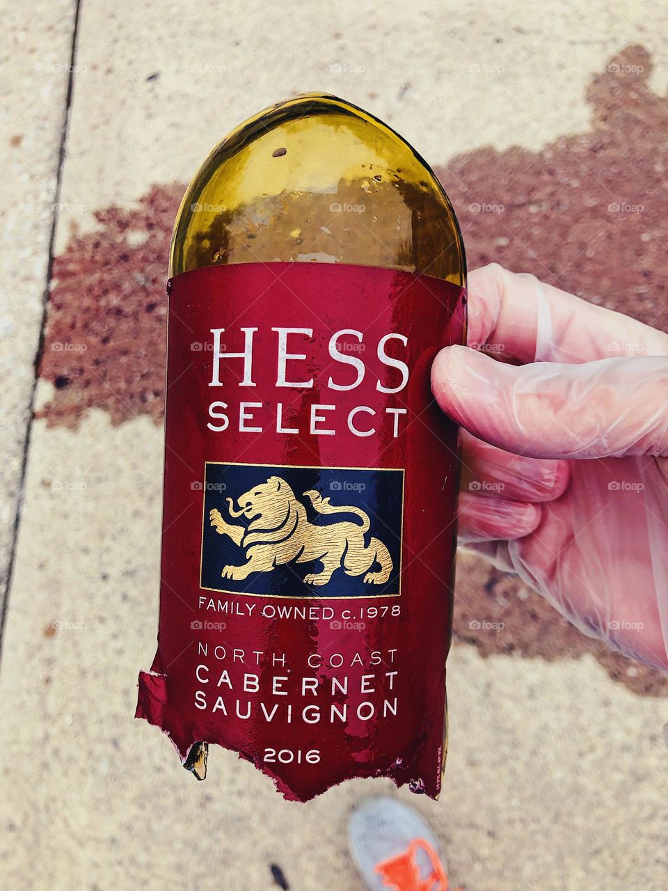 Sadness when you break a bottle of wine, sad emotions when you break a bottle of fine wine, wine spilled onto driveway and holding pieces of broken bottle, woman’s hand holding the wine broken bottle in driveway of home, Hess Select wine bottle broke