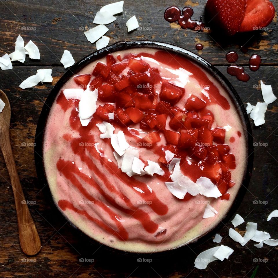 Strawberry smoothie bowl with coconut flakes on wood table