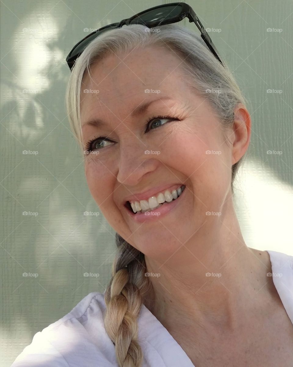 A woman smiling in the sun shade of a tree outside