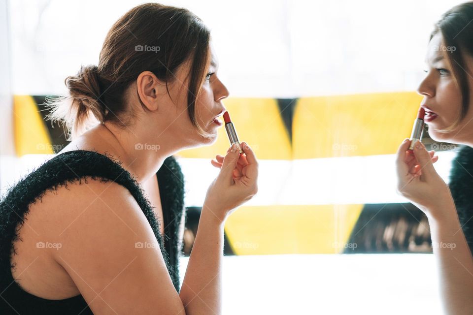Young woman doing lip makeup near mirror 