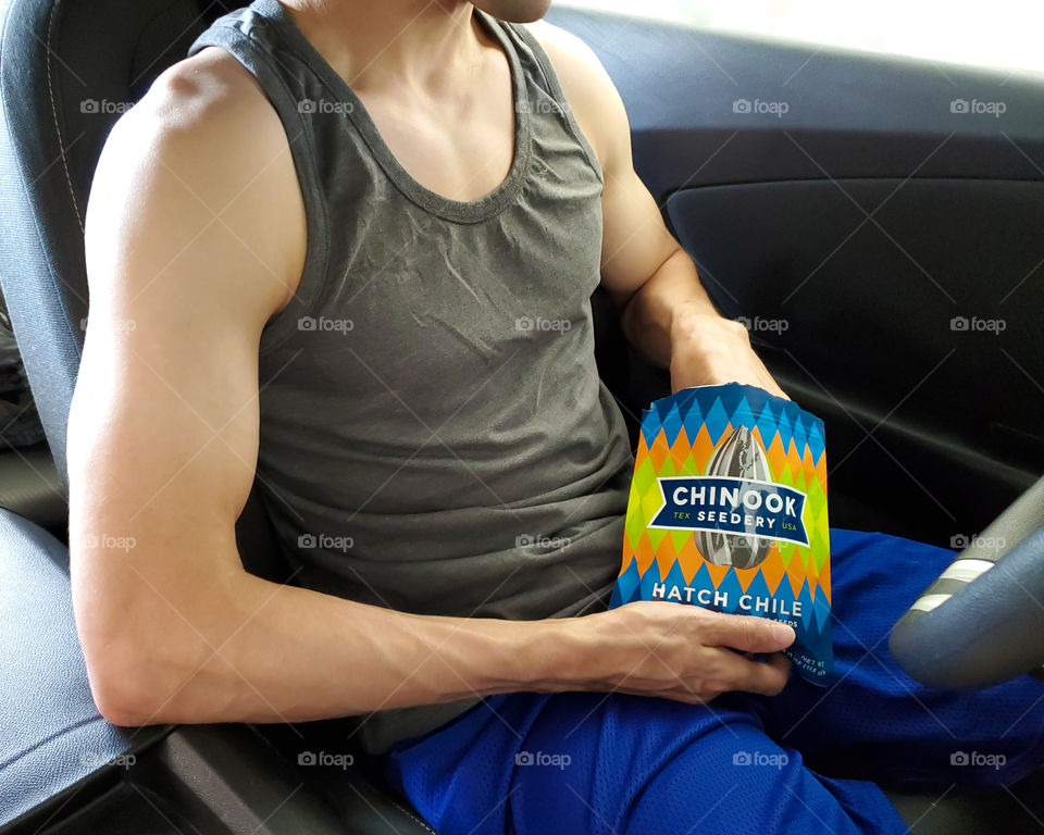 Favorite road trip snacks- Closeup of a fit man in his car eating Chinook sunflower seeds.