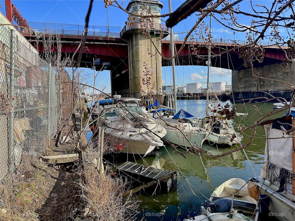 This is beautiful “Newtown Creek” by the “Pulaski Bridge” in LIC, Queens where various kinds of boats are tied to wooden planks on a narrow strip of land on the shore. 2023. Hypnotic Productions
