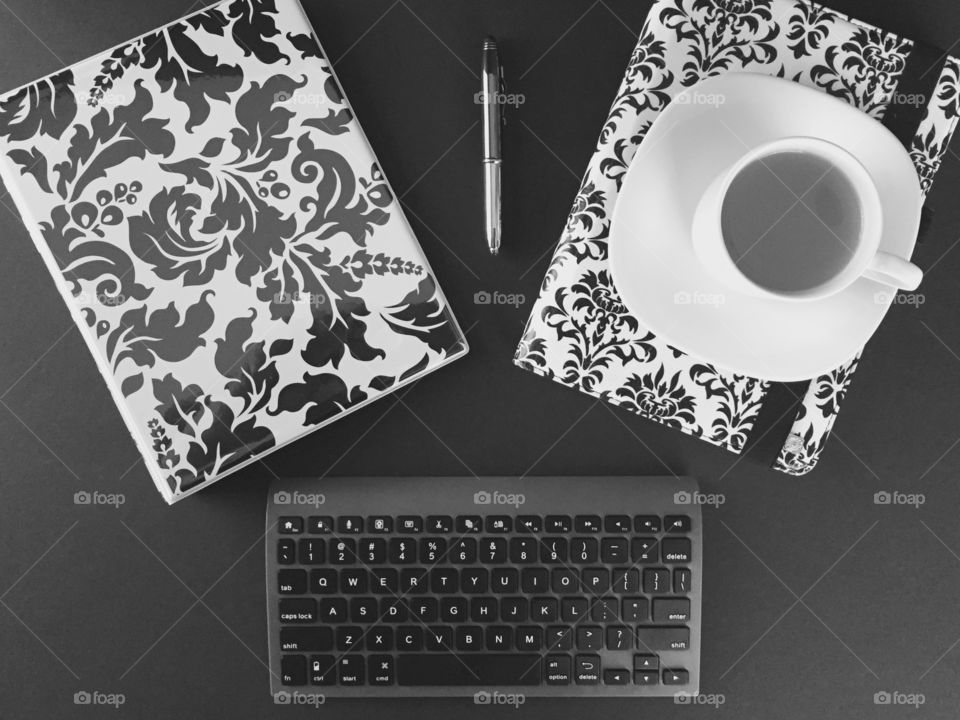 Top view desk - tablet, binder, Bluetooth keyboard, stylus, tea in cup with saucer in black and white