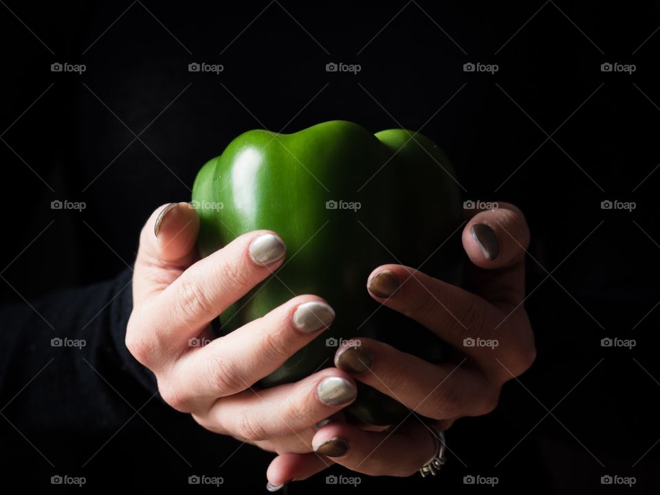 Hands holding a green pepper with a black background