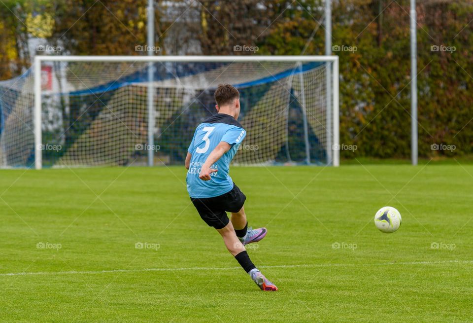 Rear view of teenage boy kicking ball at an official football match