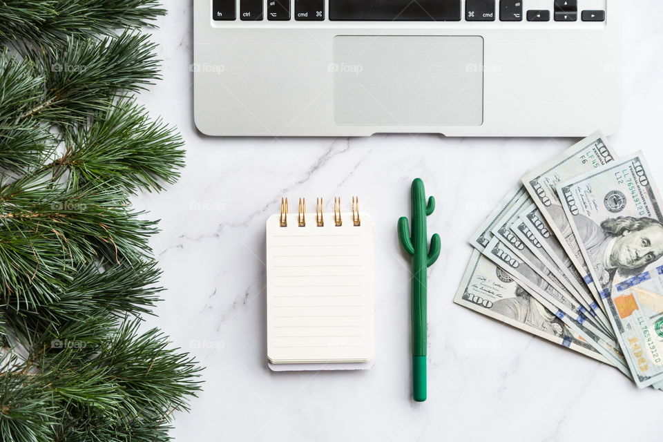 Holiday shopping. Flatlay items. Laptop, cash money one hundred dollars bill, Christmas tree , pen, notebook 