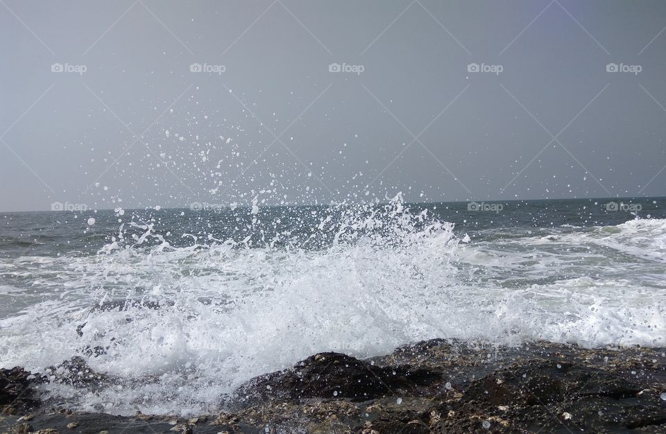 Breaking waves. Waves breaking at a rocky shore and splashing high in air along with the formed foam.