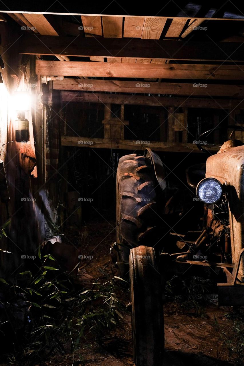 An old antique tractor sits under the shelter by the barn. 