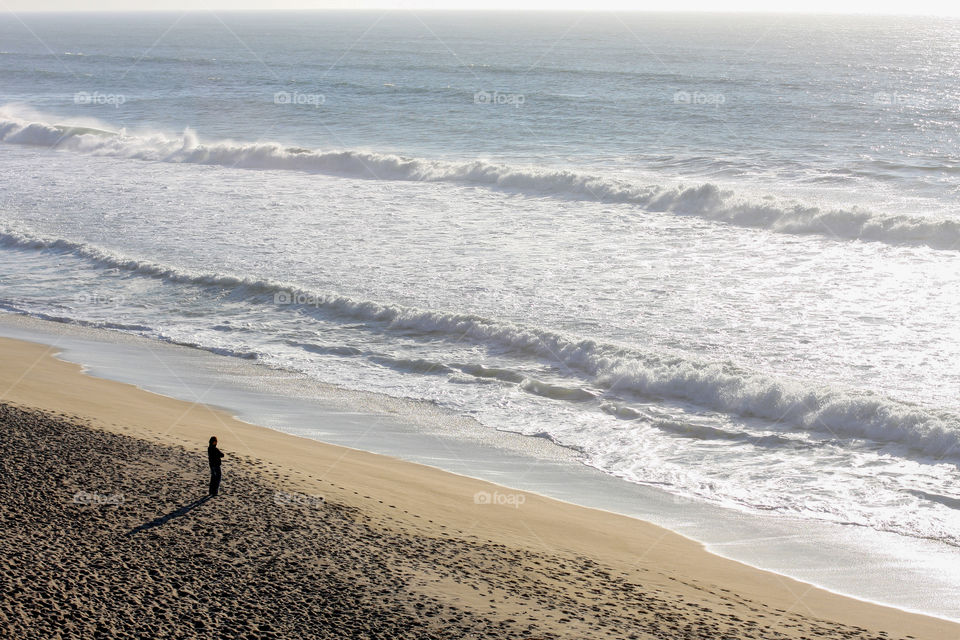A person stands alone on an empty beach and looks out at a calm ocean