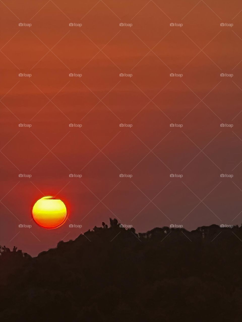 The setting sun covered in light clouds as it inches towards the horizon.