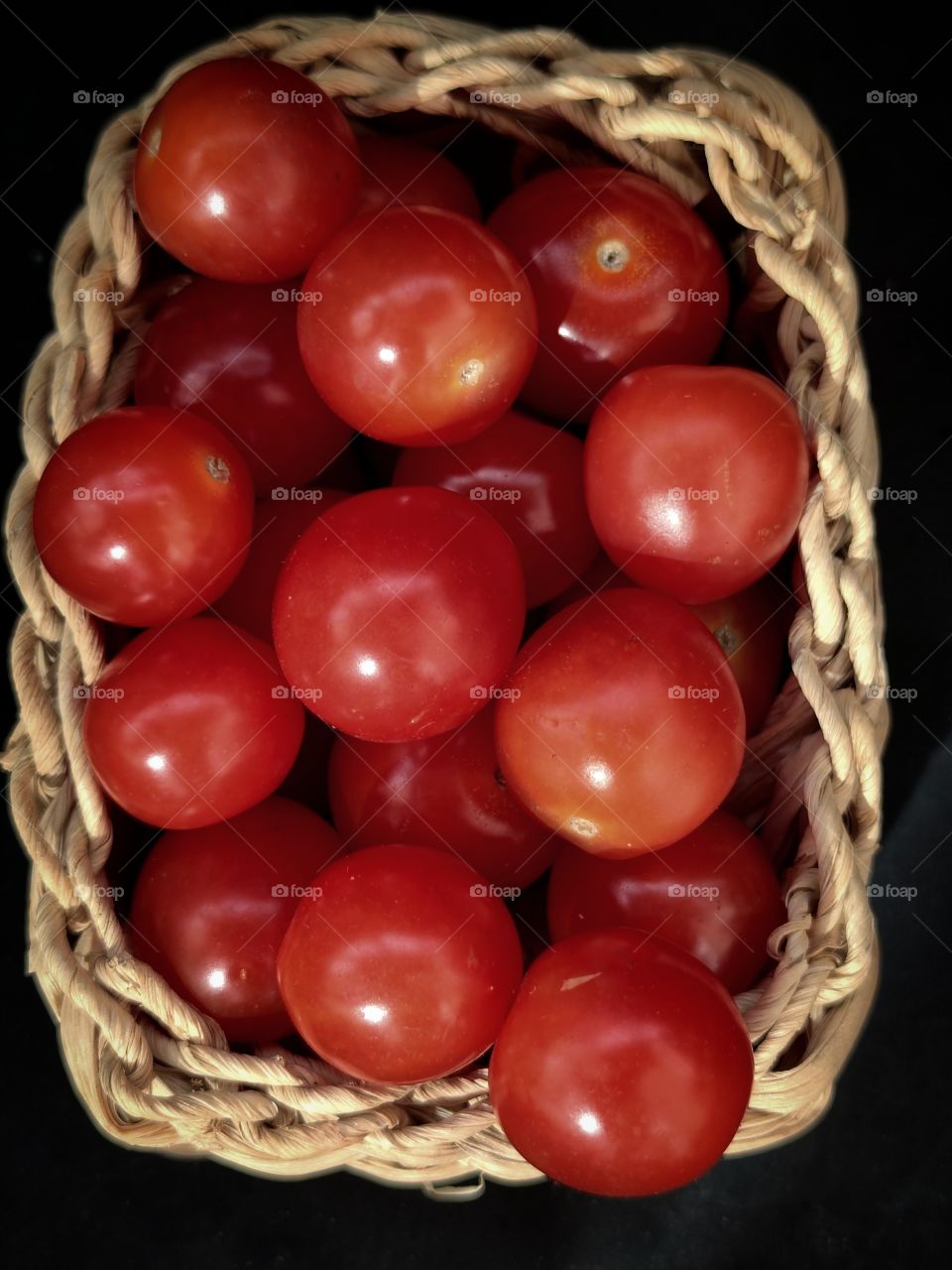 wicker wooden basket with cherry tomatoes on a black background.  view from above