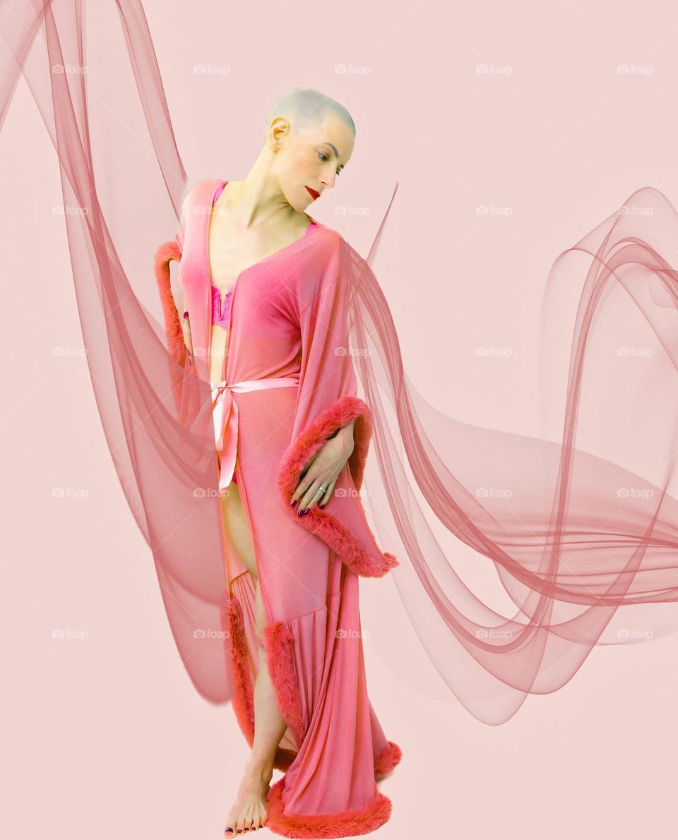 Girl in flowing dress. Ribbons and voile attached. Girl has shaved head and is dressed in pink