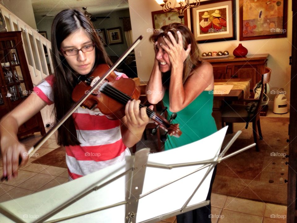 Girl playing violin while mother covers her ears