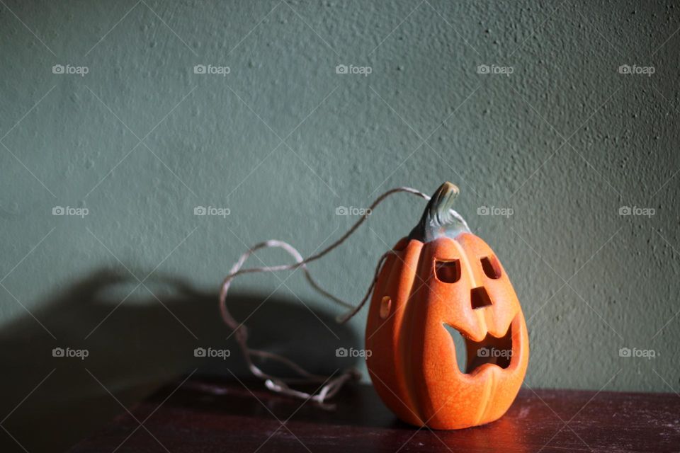 An orange Halloween decoration pumpkin with string stands on a brown cupboard in front of a green wall in the sunlight