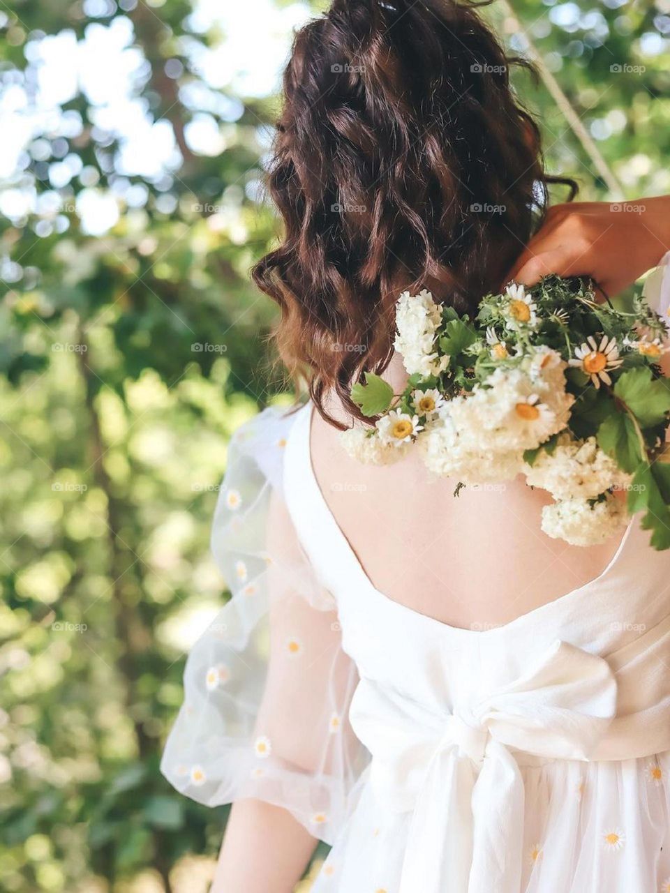 A girl as tender as flowers, under the golden light of summer, collects chamomile flowers