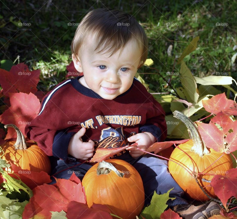 Toddler sitting in autumn leaves and pumpkins