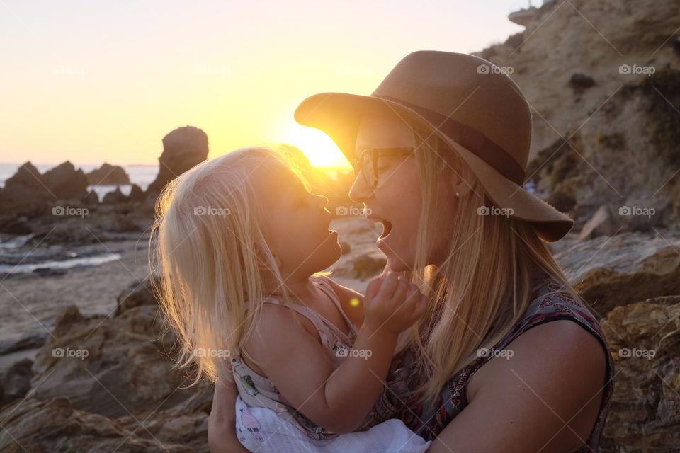 Mother and daughter kissing on the beach at sunset. 