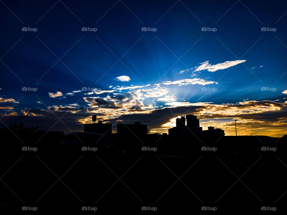 Silhouette Of The Cityscape -Cityscape Silhoutte Taken At The Time Of Sunset With Eye Catching Sun Light. Sky is looking like a dramatic and cinematic having sunrays comes out from clouds looking very attractive.It is very colourful .