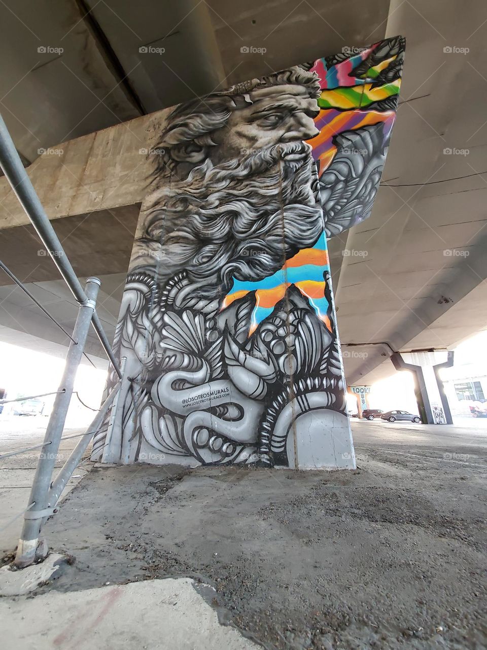 Visual street art on cement Highway pillar under highway in a parking lot. Appears to be Zeus.