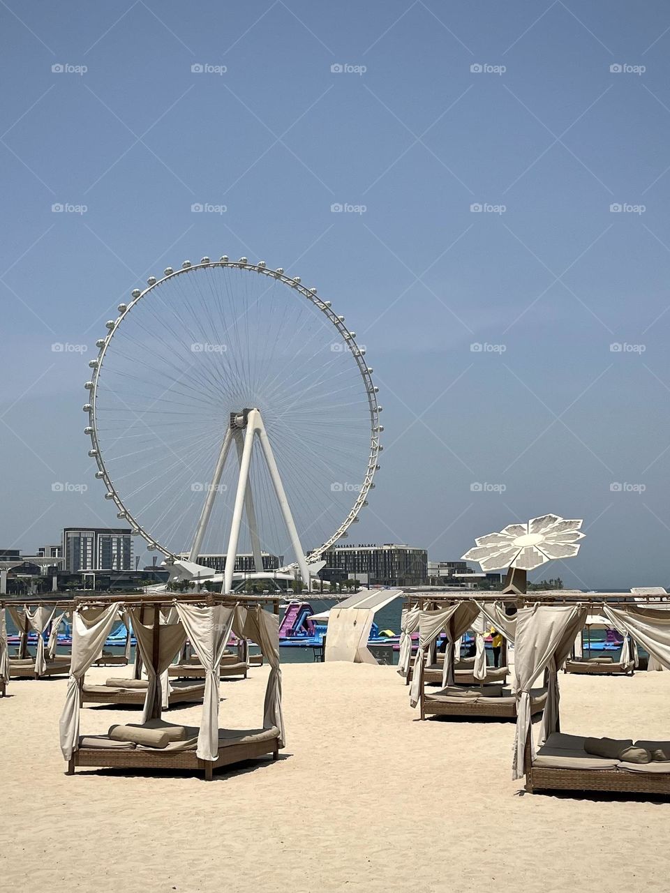 View of a Dubai beach with canopy beds on the sand and a Ferris wheel in the background