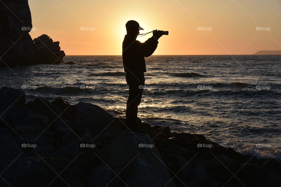Amateur photographer enjoying seascape through his lens during sunset.