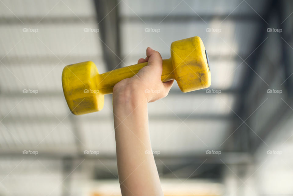 Kid working out with dumbbells  in the sports hall of the club. Child hand holding yellow dumbbell