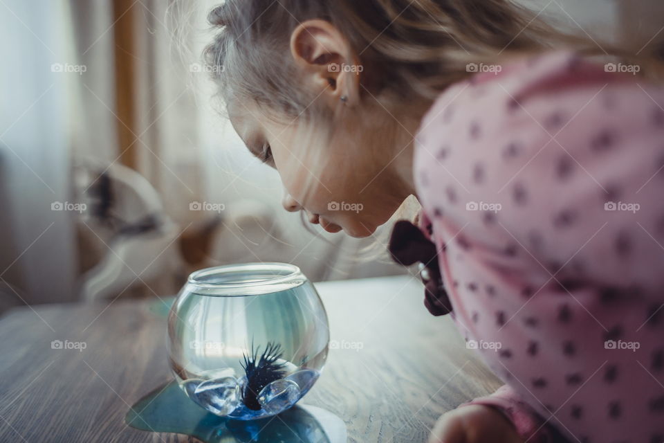 Little girl with fish in round aquarium at home