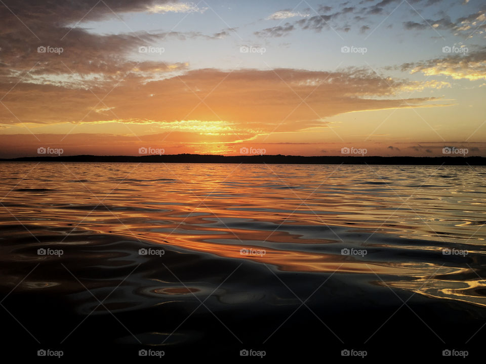 Colorful sunrise with illuminated clouds over Jordan Lake near Apex North Carolina with gold, yellow, and orange shimmering on the ripples. Raleigh and Triangle area. 