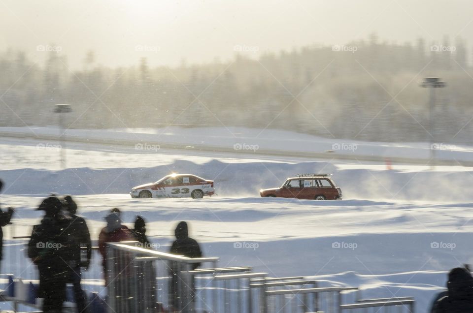 Winter drift competitions on a sunny day. Two bright cars are driving fast on a winter highway.